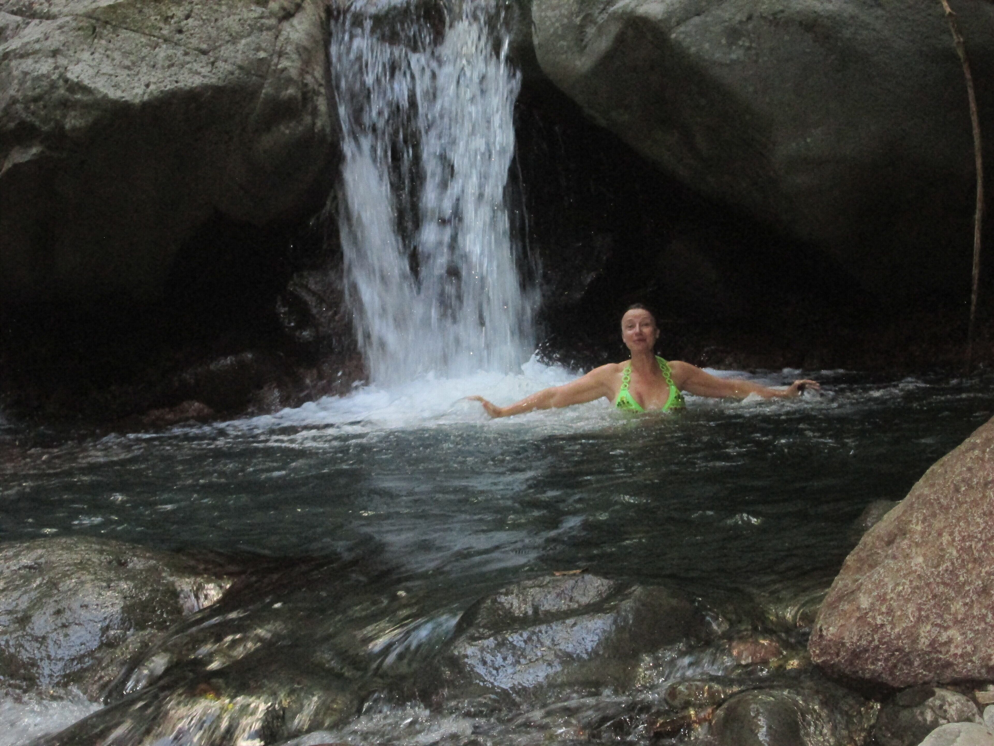 Une personne portant un maillot de bain vert, dans un environnement naturel avec des rochers et une cascade.