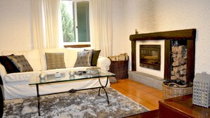 A cozy living room with a sofa, glass coffee table, fireplace, and a view of the outdoors.