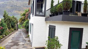 A white building with a balcony, green shutters, and a stone pathway leading to a door.