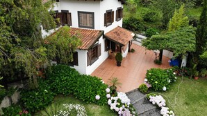 A two-story white house with a tiled roof, surrounded by lush greenery and a well-maintained garden with various plants and flowers.