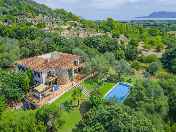 Una casa grande con piscina, rodeada de exuberante vegetación y vistas al mar.