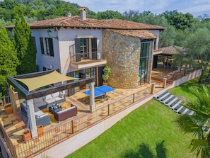 Una casa de dos pisos con fachada de piedra, un balcón y un patio con mobiliario exterior.