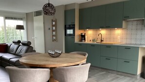 A modern kitchen with green cabinets, a wooden dining table, and a built-in oven.