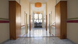Un pasillo con puertas de madera, suelo de mármol y vistas a un balcón.