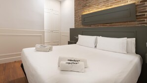 Una cama bien tendida con sábanas blancas y dos toallas con texto, una pared de ladrillo y una puerta blanca en una habitación de hotel.
