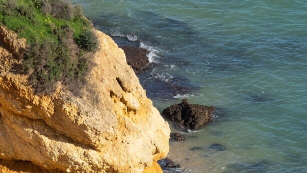 Uma praia com uma grande formação rochosa e água azul cristalina.