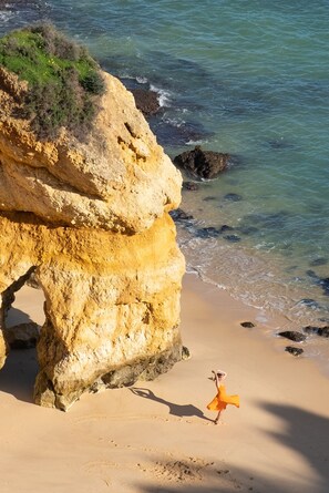 A beach with a large rock formation and clear blue water.
