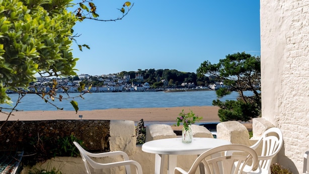 A terrace with white plastic chairs and a table, overlooking a body of water with a town in the background.