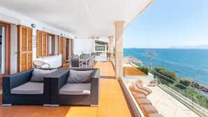 A balcony with a sofa, dining table, and chairs, overlooking a coastal view.