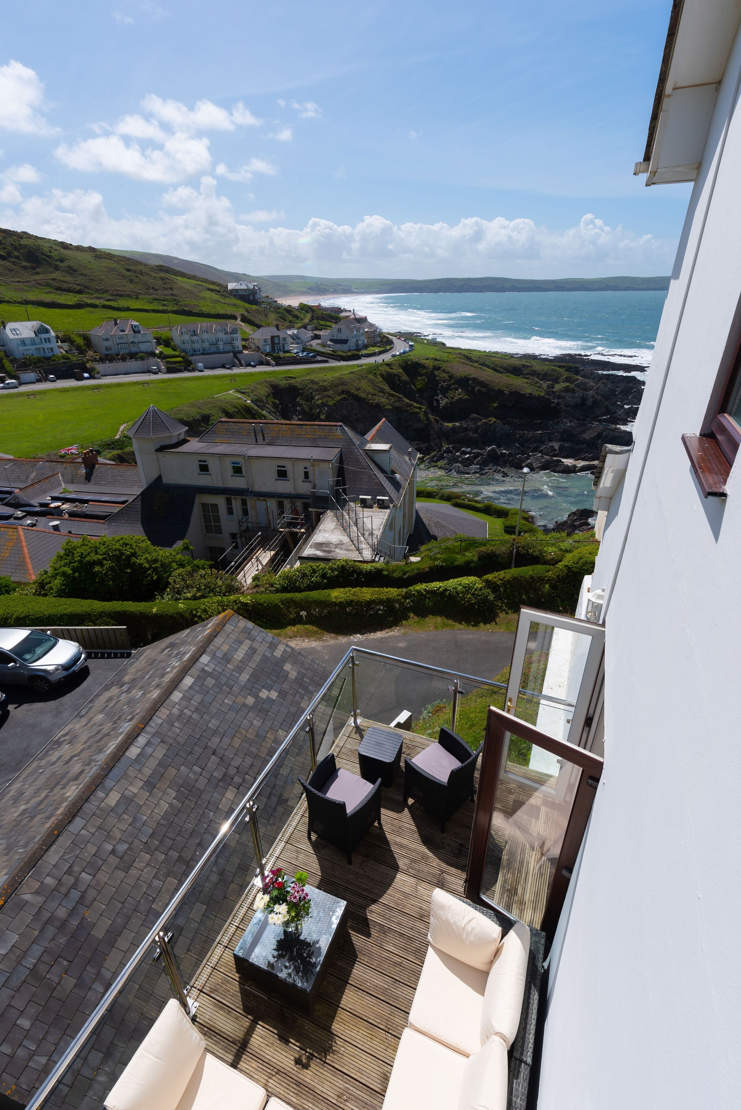 Un balcón con mobiliario exterior que da a una zona costera con casas y vistas al mar.