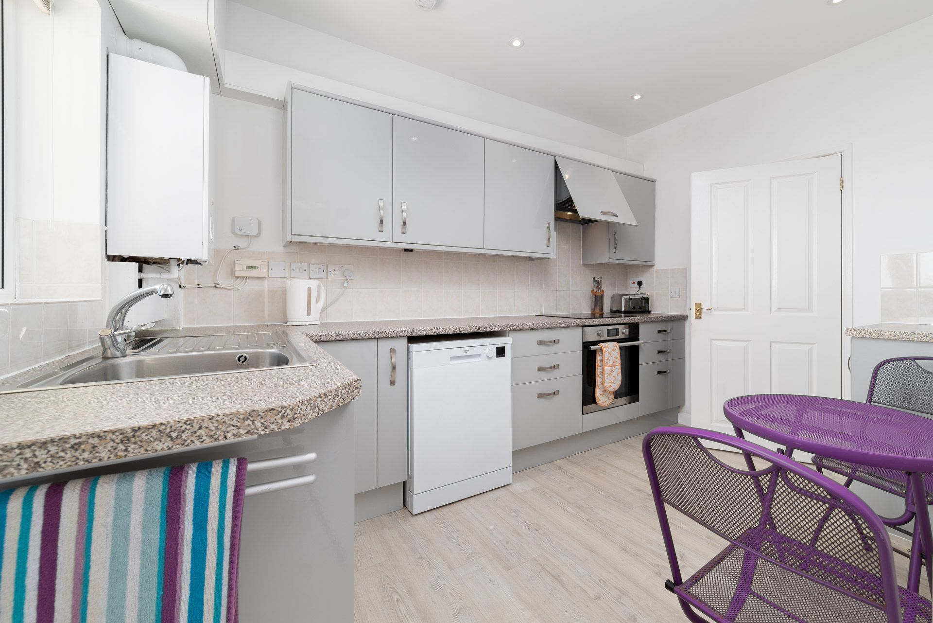 A modern kitchen with white cabinets, a granite countertop, a dishwasher, and a purple metal chair.