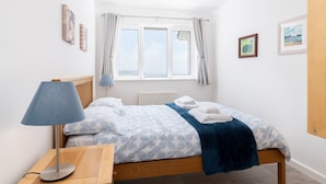Un dormitorio con cama, mesita de noche, lámpara, ventana con cortinas e imágenes enmarcadas en las paredes.