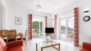 Una sala de estar moderna con sofás de cuero rojo, una mesa de centro de vidrio, un televisor de pantalla plana y ventanas amplias con cortinas rojas.