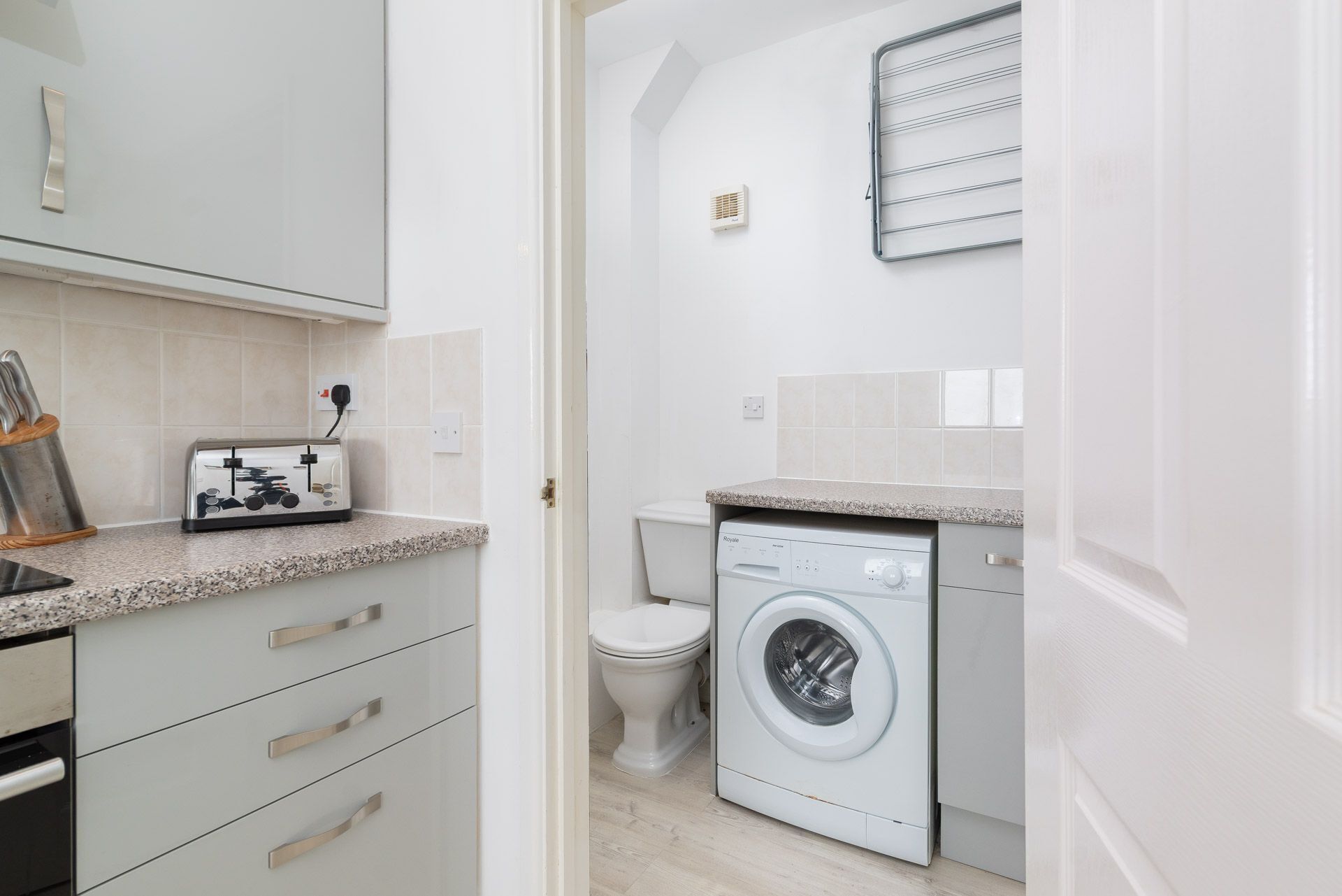 A modern kitchen with a built-in washing machine, a toaster, and a small window with blinds.