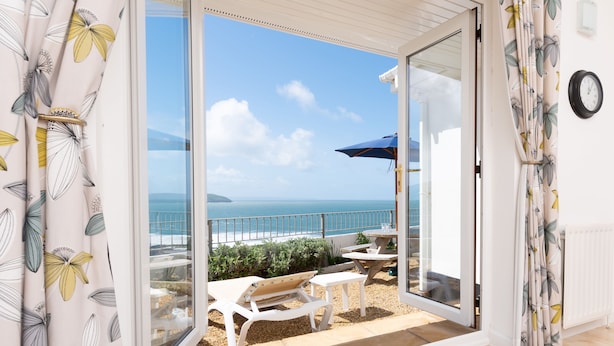 Un balcón con vista al mar, muebles blancos y un reloj en la pared.
