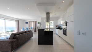 Een moderne woonkamer met een groot raam, een bank en een keuken met witte kasten en apparatuur.