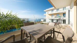 Een balkon met een tafel en stoelen, met uitzicht op een zwembad en een modern gebouw met meerdere balkons.