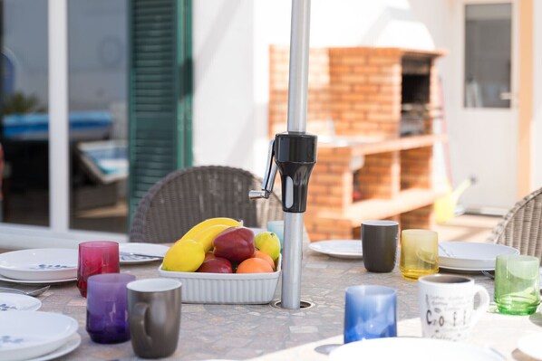 Una mesa con un frutero, un dispensador de agua y tazas y platos de varios colores.