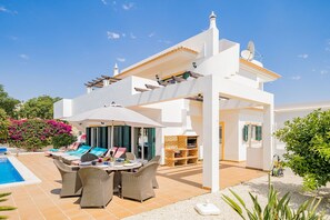 Una villa blanca con piscina, mobiliario de exterior y zona de barbacoa.