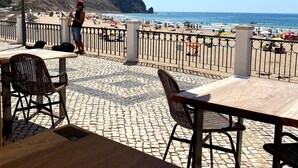 An outdoor seating area with tables and chairs, a musician playing a saxophone, and a view of the beach and ocean.