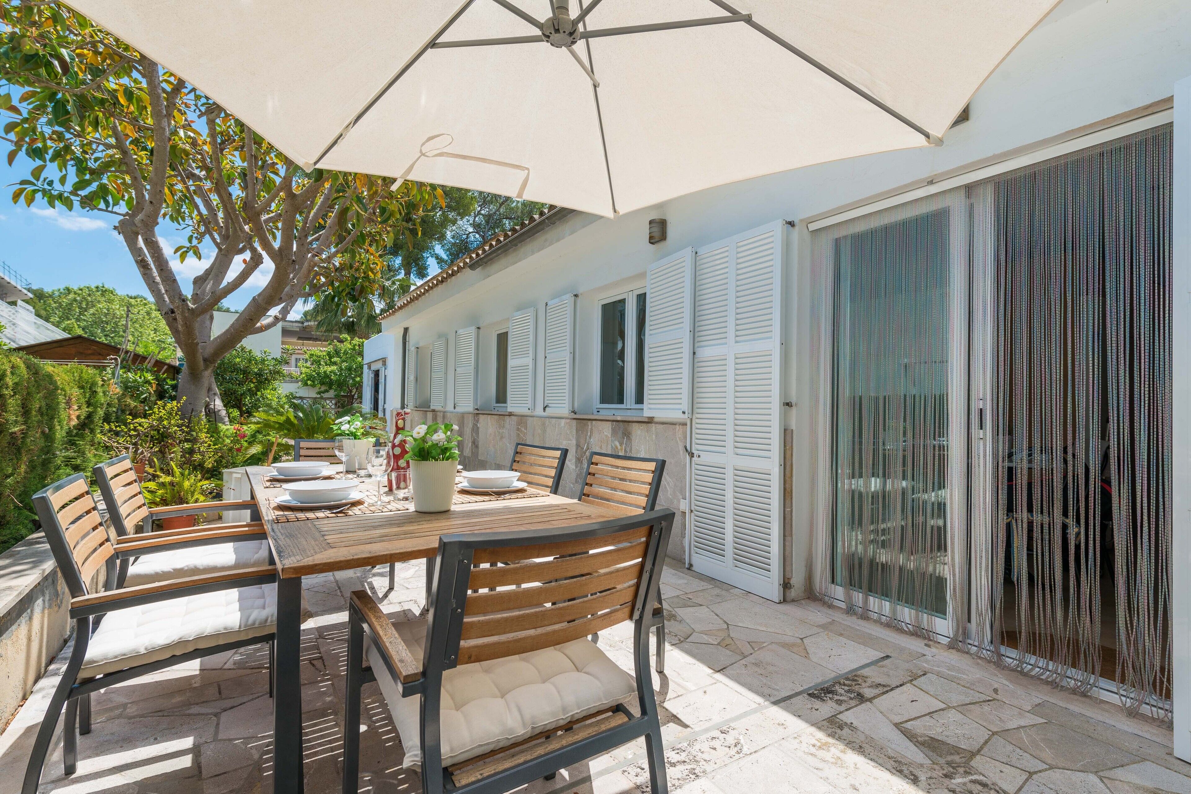 An outdoor patio with a wooden table and chairs, a large umbrella, and a sliding glass door.