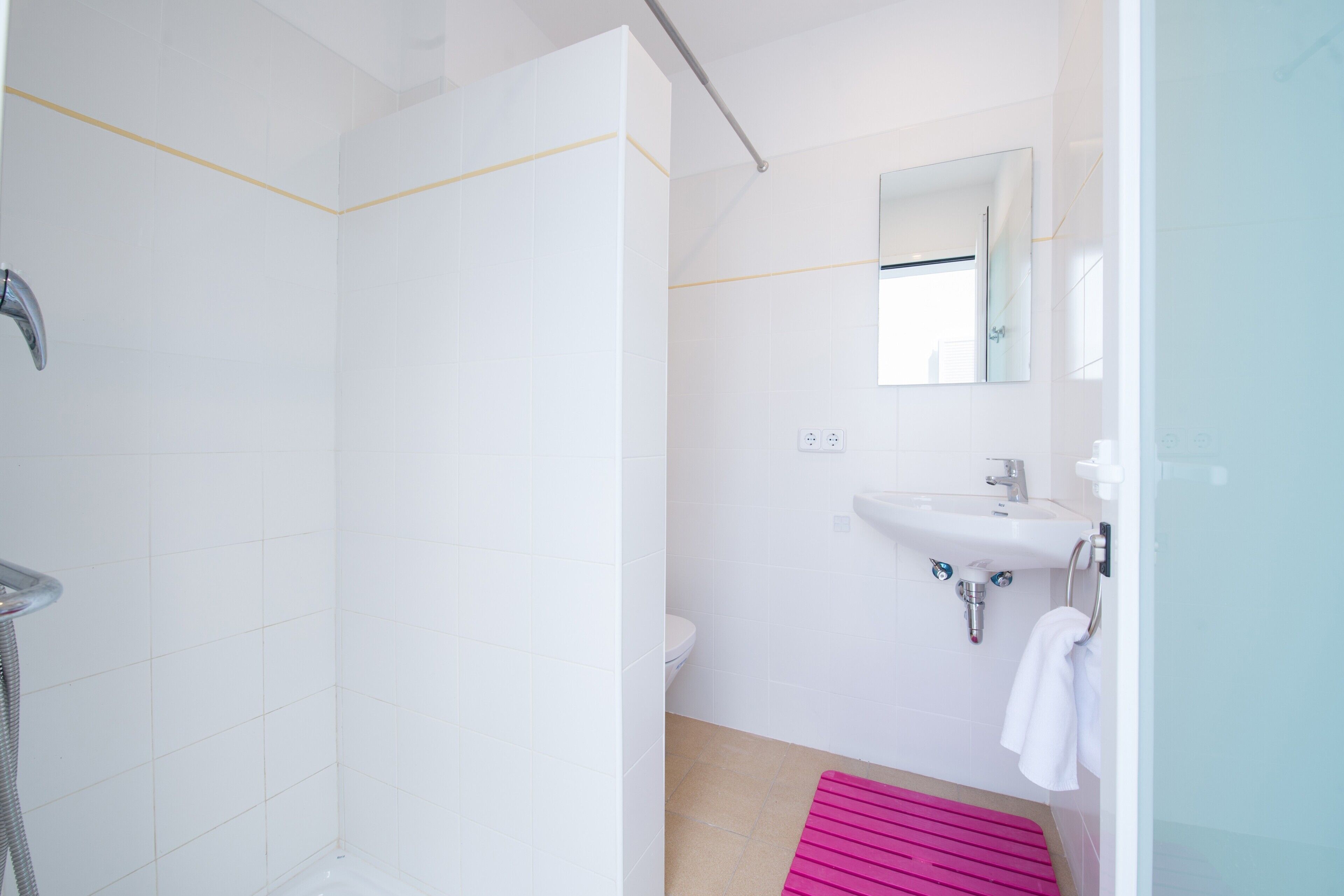 A bathroom with a shower, toilet, sink, and a mirror.