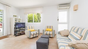 A living room with striped sofas, a TV on a stand, and a window with curtains. - CAN GARRETA - Beautiful holiday home near the beach. Free WiFi (Alcúdia)