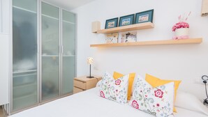 A bedroom with a bed, a wardrobe, a bedside table with a lamp, and shelves with framed pictures and a vase. - CAN GARRETA - Beautiful holiday home near the beach. Free WiFi (Alcúdia)