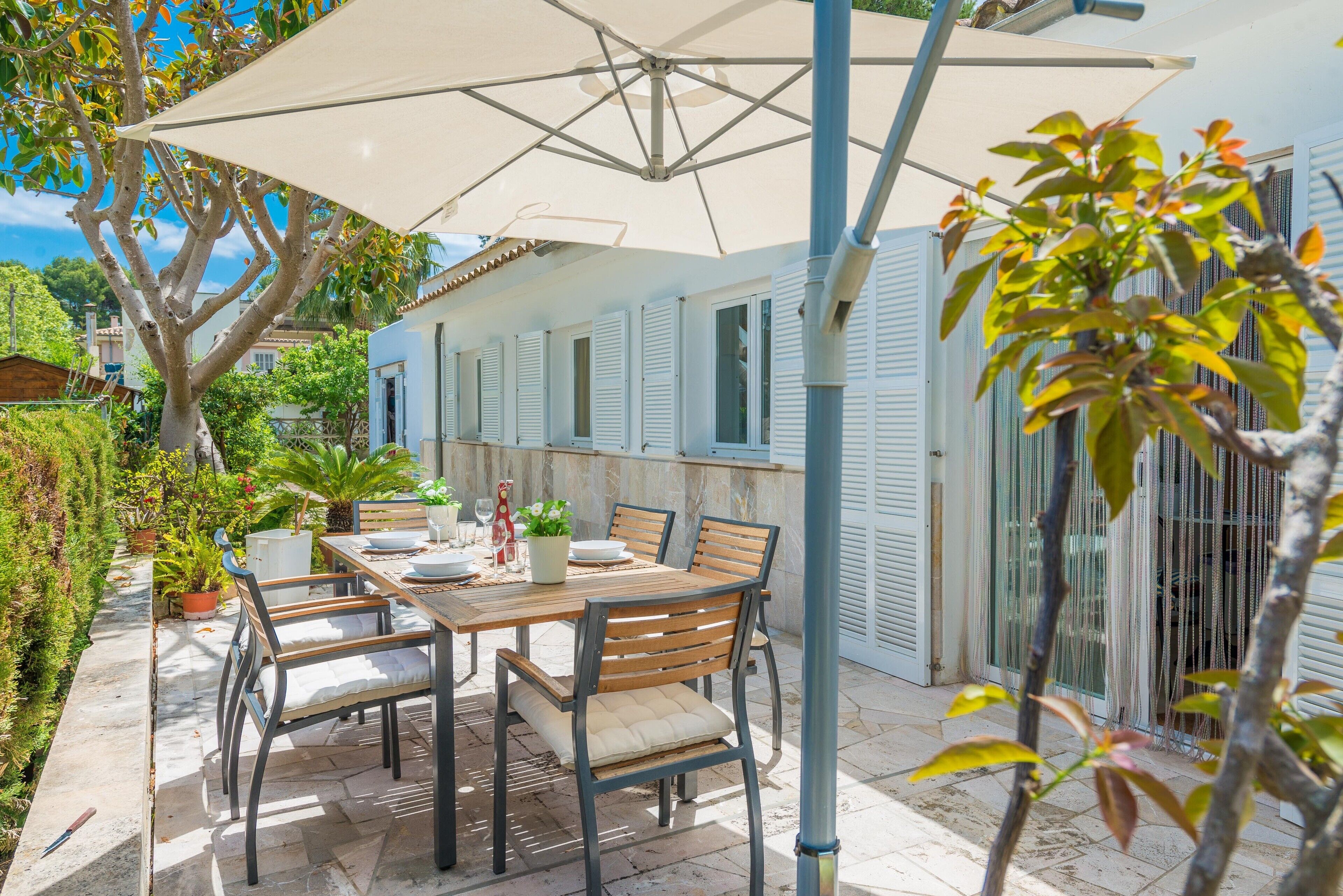 An outdoor patio with a table and chairs, a large umbrella, and potted plants.