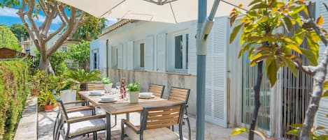 En udendørs terrasse med et bord, stole, en stor parasol og plantekasser.