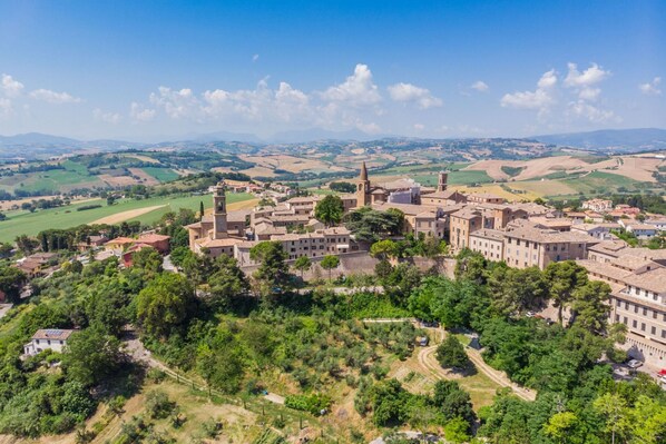 A historic town with a prominent church tower, surrounded by lush greenery and rolling hills in the background. - Villa Azzurra by Anita Villas (Mondavio)