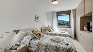 Une chambre avec deux lits, une table de chevet, un bureau, une lampe, une fenêtre avec vue et un luminaire au plafond.