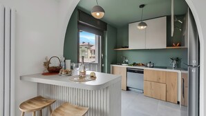 Une cuisine moderne dotée d’un îlot central, de tabourets en bois et offrant une vue sur l’extérieur à travers une arche.