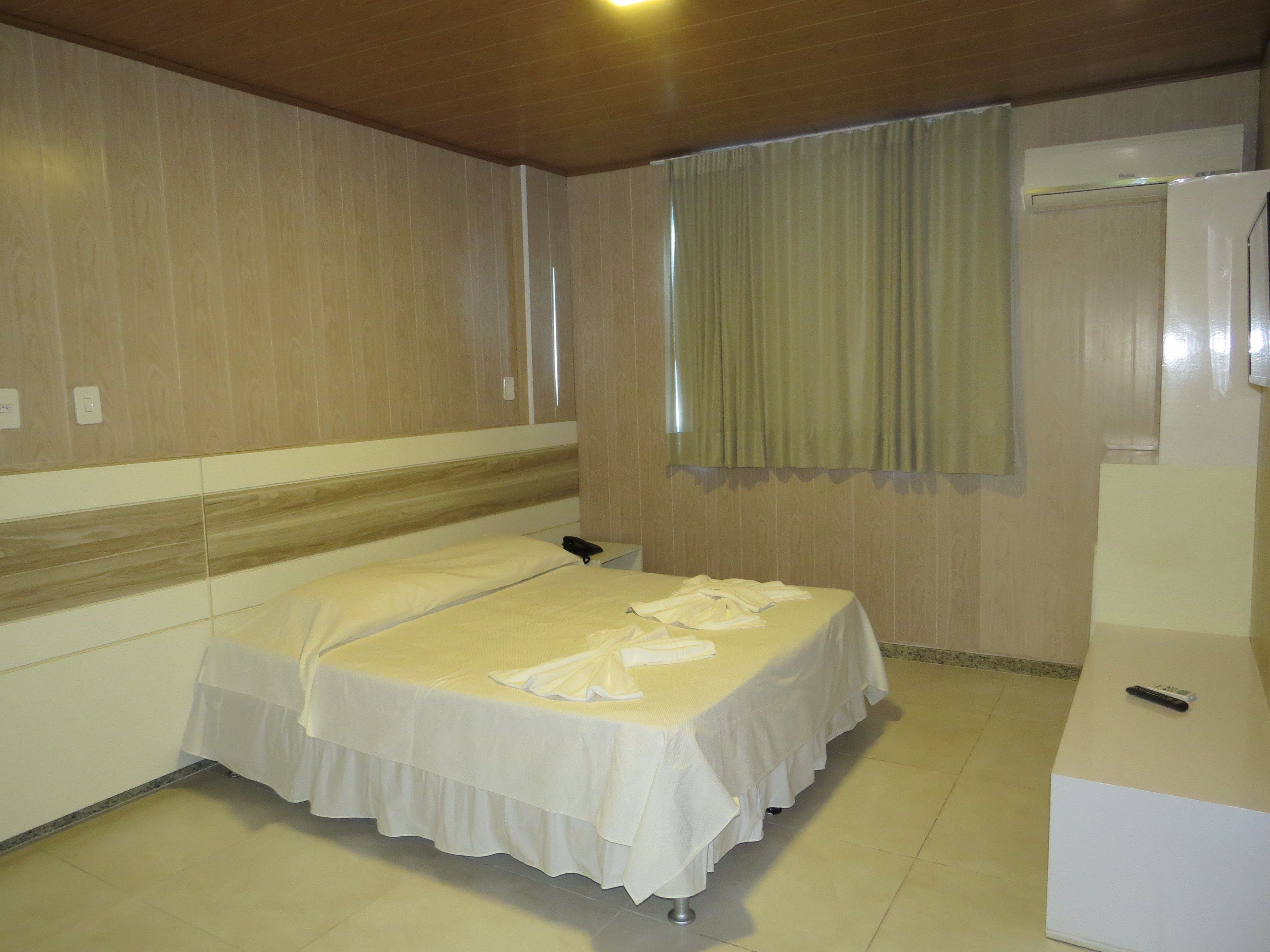 A hotel room with a single bed, a bedside table, a mirror, and a window with curtains.