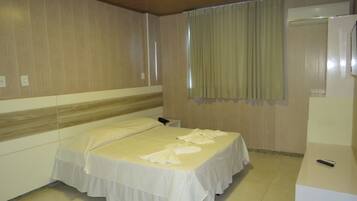 A hotel room with a single bed, a bedside table, a mirror, and a window with curtains.