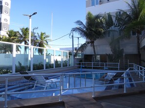 Ein Pool mit Fliesen umgeben von Palmen und einem Gebäude mit großen Fenstern.
