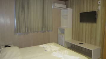 A hotel room with a bed, a desk, a flat-screen TV, and an air conditioning unit.