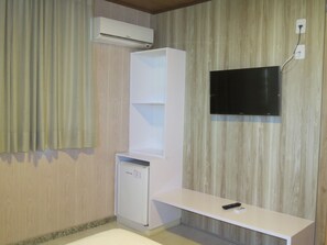 A room with a built-in mini-fridge, a white TV mounted on the wall, and a white shelf unit. - Farol Plaza Hotel (Aracaju)
