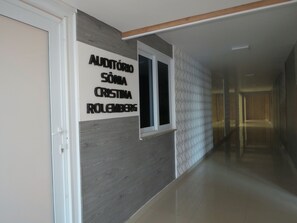 Un couloir avec une pancarte sur le mur indiquant : « AUDITÓRIO SÓNIA CRISTINA IROLEMBERG ».