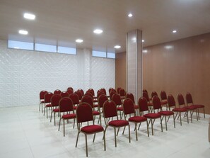 Ein Konferenzraum mit Reihen roter Stühle und einer weißen Wand mit Struktur.