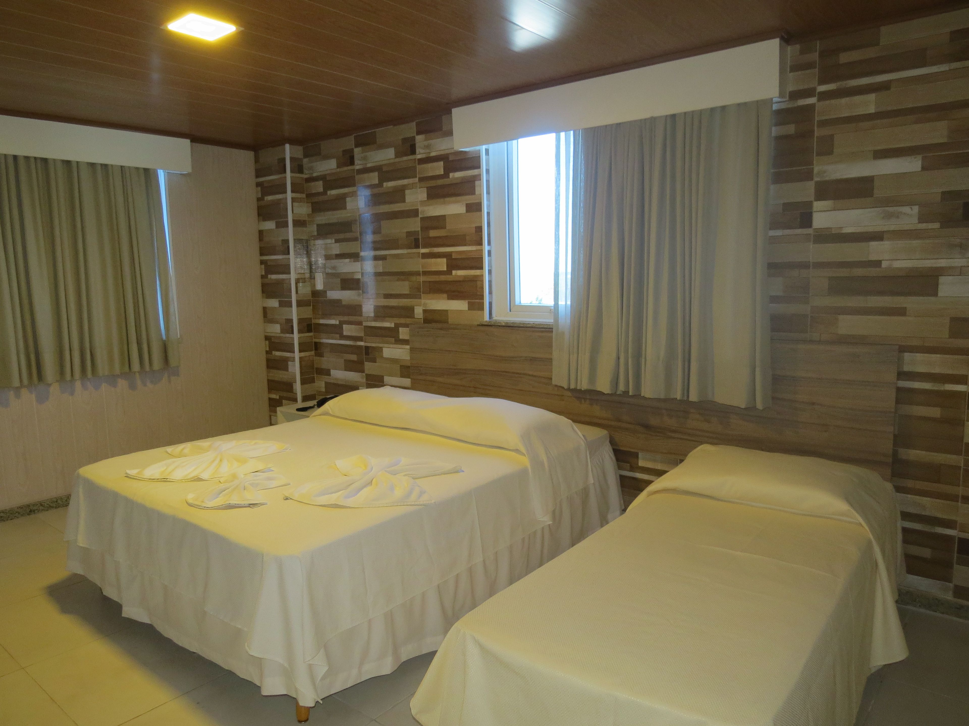 Habitación de hotel con dos camas, techo de madera, pared de piedra y ventana con cortinas.