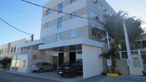 Un hotel de varios pisos con fachada plana, varias ventanas y un estacionamiento con dos coches.