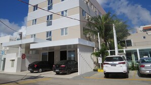 Un edificio de hotel de varios pisos con fachada plana, espacios de estacionamiento y una palmera en frente.