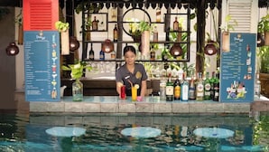 Zona de bar con carta de bebidas, varias botellas y una piscina con objetos flotantes.