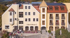 Ein Hotel im klassischen europäischen Baustil, mit einem markanten Eingang, einer Treppe, einem Balkon und dem Schriftzug "Hotel Burzer".