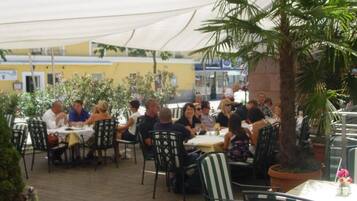 An outdoor dining area with tables and chairs, surrounded by potted plants and a palm tree.