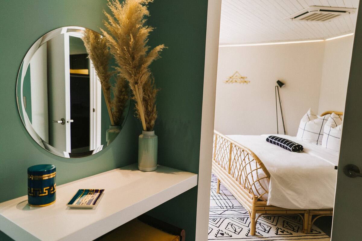 A room with a bed, a bedside table, a mirror, and a wall-mounted shelf.