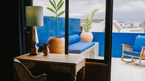Ein Zimmer mit einem Holztisch, einem Sessel, einer Couch, einer Lampe und Blick auf die Stadt durch große Fenster.