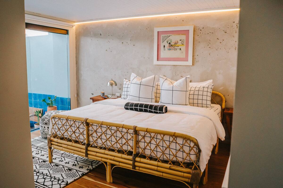 A bed with a woven headboard, a bedside table, a lamp, and a framed picture on the wall.