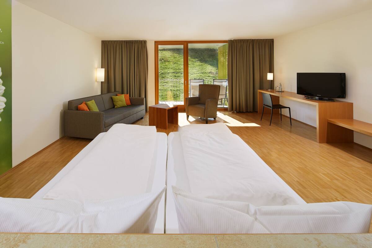 A hotel room with a large bed, a sofa, a desk, a chair, and a television.